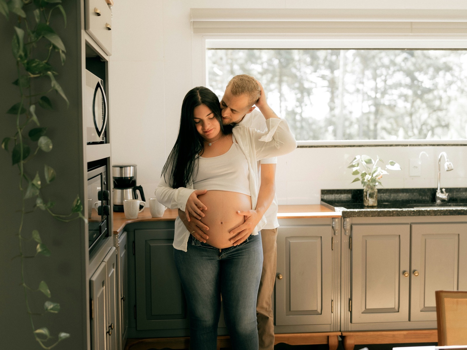 Ein werdendes Elternpaar steht gemeinsam in der Küche und hält den Babybauch